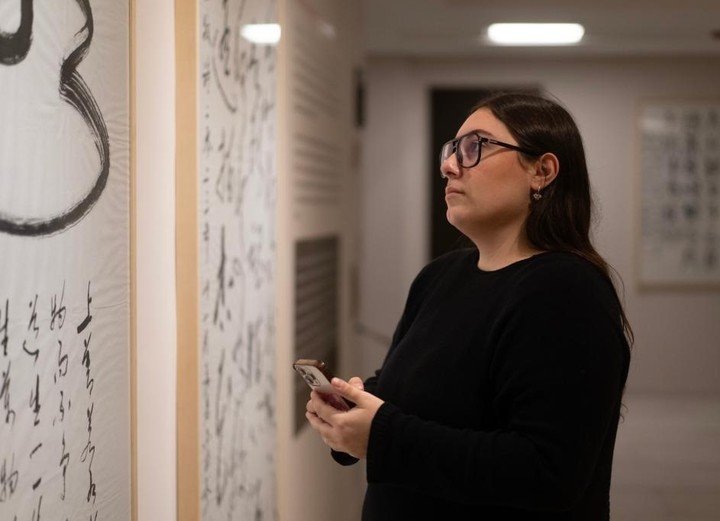Una mujer tomando una fotografía a obras de caligrafía china exhibidas durante la muestra "Poéticas del movimiento. Arte, escritura y caligrafía en China". (Xinhua/Martín Zabala)