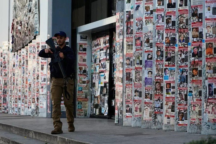 Un agente de policía pasa por delante de una pared cubierta con carteles con el rostro de desaparecidos, frente a la Fiscalía Especializada en Investigación de los Delitos de Desaparición Forzada, en Guadalajara, México, el 25 de febrero de 2026. (Marco Ugarte / Associated Press)
