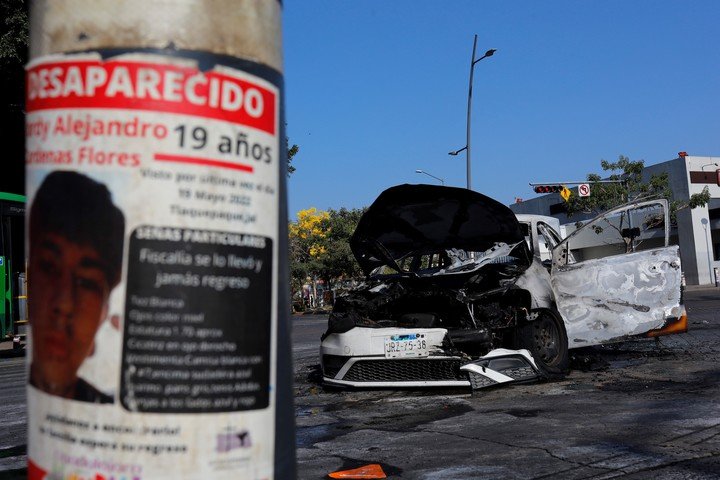 Fotografía que muestra un cartel de una persona desaparecida y un vehículo incendiado, en una vía de Guadalajara (México). EFE/ Francisco Guasco